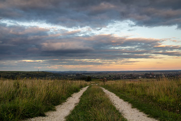 Dirt road among dark fields at sunset with dramatic cloudscape.