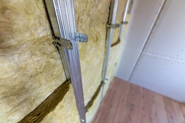 Wall of a room under renovation with mineral rock wool insulation and metal frame prepared for drywall plates.