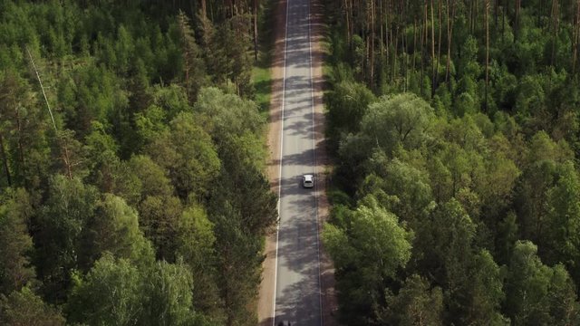 One white wagon car driving in  freeway through dense forest corridor at summer sunny day - Aerial drone view