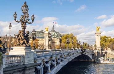 Fotobehang Pont Alexandre III Beroemde Pont Alexandre III-brug op zonnige herfstdag. Daarachter is het dak van het Grand Palais met de Franse vlag die afzwaait tegen de wolken
