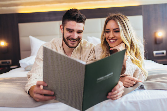 Couple in hotel room reading room service menu together in bed