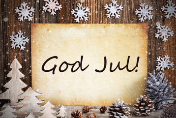 Fototapeta na wymiar Old Paper With Swedish Text God Jul Means Merry Christmas. Christmas Decoration Like Tree, Fir Cone And Snow. Brown Wooden Background