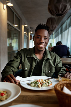 Young African American Man Is Eating In A Restaurant And Enjoying Delicious Food