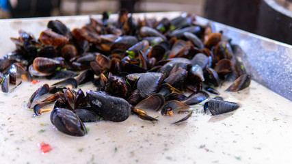 Fresh mussels at grill pan. Seafood barbecue outdoors. Picnic healthy food, mussels in shells.Plenty of mussel shells cooking at large metallic pan.