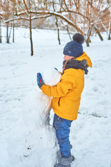 Fototapeta na wymiar little girl sculpts a snowman in winter