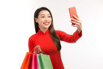 Fototapeta na wymiar Shopping on lunar New Year, beautiful woman holding bags and selfie, dress in red traditional costume for Vietnamese people.