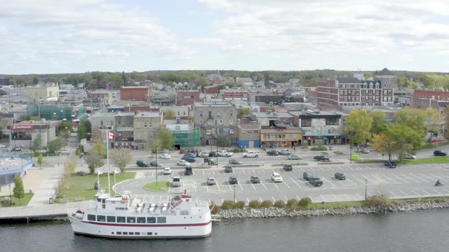 Flying around tour boat docked in the Lake of the Woods, Kenora, Ontario, Canada. parking lot anc houses in the background. Panoramic view 4k drone footage from right to left.