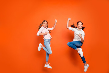Fototapeta na wymiar Full length photo of positive two blonde brown hair girlfriends with long tails jump raise fists feel content wear casual outfit isolated over orange color background