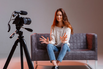 Young teen girl vlogger makes a video stream on the couch at home. A video camera on a tripod.