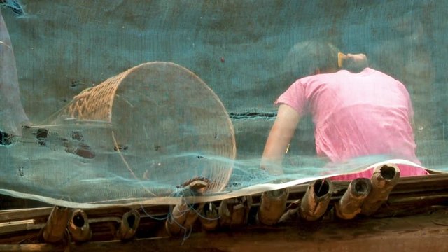 A daylight closeup shot of a local woman combing her hair inside the house with an open wall and surrounded by a green mosquito net.