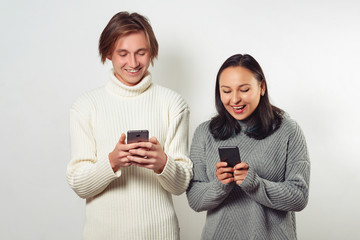 Happy young guy and girl with smartphones in hand, chatting with each other and laughing. on white