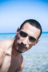 young muscular man resting and posing on the beach