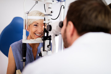 Optometrist examining senior woman in modern ophthalmology clinic - obrazy, fototapety, plakaty