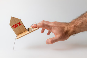 The concept of Bank investments and risks. A man's hand falls into a mousetrap, with a cardboard insert with the text TAX