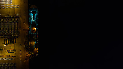 Overhead view of a vehicle transport terminal at night with a car transport vessel and parked cars...
