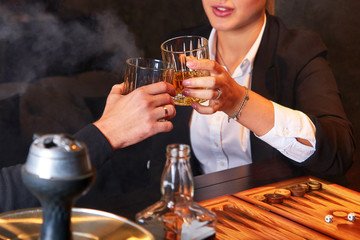 Woman and man drinking whiskey, smoking hookah and playing backgammon.