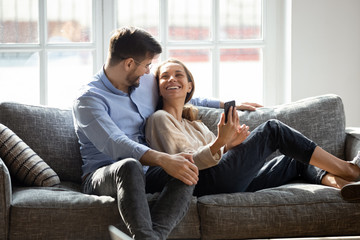 Laughing millennial mixed race woman showing funny video to husband.