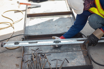 Workers are using a ruler to measure the distance between the points of the piece that must be welded on the angle steel frame. Wearing black-brown leather gloves With a wrought iron rod beside him