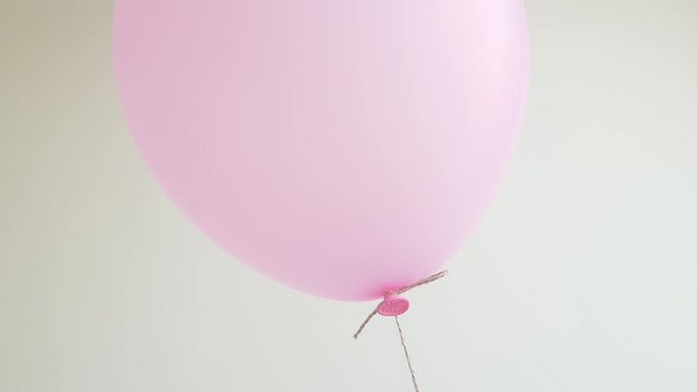 Light helium balloon in pink floating against off white wall. Minimalist design template for Pink October breast cancer awareness month campaign or birthday party celebration.