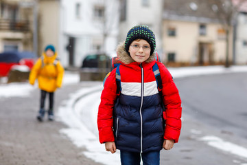 Little school kid boy of elementary class walking to school during snowfall. Happy child and student with eye glasses backpack in colorful winter clothes. schoolkid in yellow jacket on background