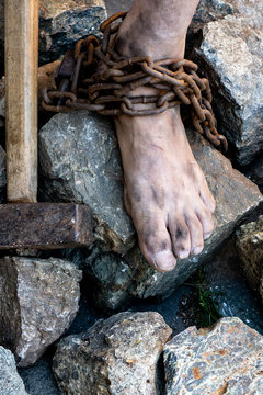 Dirty slave legs in chains among stones. Slave in an attempt to free himself. The symbol of slave labor