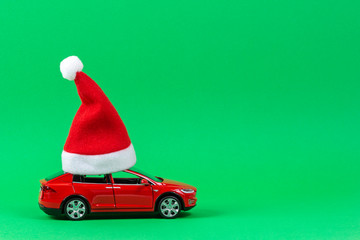 Red toy car with Christmas Santa Claus hat on light green background
