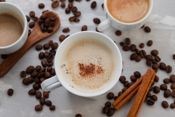 cups of coffee with milk and grains on ceramic background