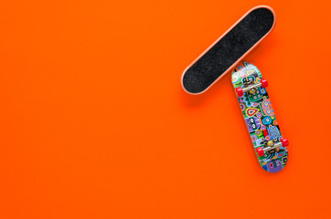 Two mini skateboard toys with red wheels on an orange background. Teenagers leisure concept. Flat lay. Copy space
