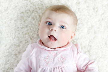 Close-up of a two or three months old baby girl with blue eyes. Newborn child, little adorable smiling and attentive girl looking surprised at the camera. Family, new life, childhood concept.