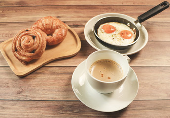 Top view of break fast set ,, cup of coffee fried eggs , danish pastry and Croissant on wooden background.