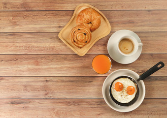 Top view of fried eggs in pan,orange juice , cup of coffee and  danish pastry and Croissant on wooden background.