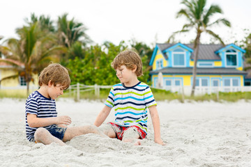 Two little kids boys having fun on tropical beach, happy best friends playing, friendship concept. Siblings brothers, twins in family look with palms on background. Family vacations on Seychelles.