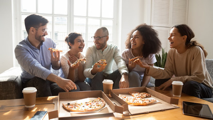 Overjoyed young diverse buddies eating ordered pizza for home party.