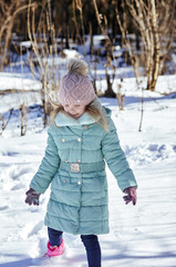 Little kid girl in colorful clothes playing outdoors. Active leisure with child in winter on cold days. Happy child having fun with snow