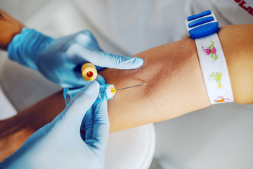 Close up of lab assistant with sterile rubber gloves taking blood sample from patient.