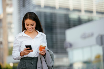 Fototapeta na wymiar Beautiful businesswoman outdoors. Young woman on coffee break typing message on smart phone. 