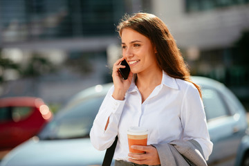 Beautiful businesswoman outdoors. Young woman on coffee break. Beautiful woman talking on smart phone. 