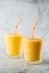 Two glasses of yellow banana, orange , mango smoothies or juice fruit isolated on bright marble background. Overhead view, copy space. Advertising for cafe menu. Vertical photo.