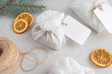 Christmas presents wrapped with white furoshiki fabric, labels and dried orange slices. Eco friendly gift.