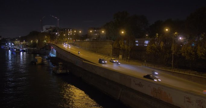Steady shot of a Paris road by night (looks like a highway). Seine river on the left. Professional cinematic low light footage.