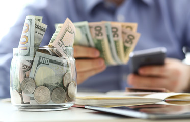 Rich jar full or US banknotes and coins with businessman arms in background
