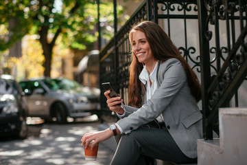 Fototapeta premium Beautiful businesswoman on coffee break using phone. Young businesswoman outdoors. 