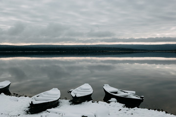 boats under the snow on the shore of a mountain lake in late autumn