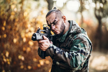 A soldier in camouflage uniform and painted face is targeted. Holds a rifle. Photo at half height. Airsoft