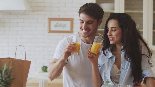 Happy couple drinking orange juice at kitchen. Closeup couple flirting at home.