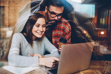 Positive excited young couple in love watching live stream on website via high speed internet connection on laptop computer.Amazed two hipsters enjoying online broadcasting on modern netbook