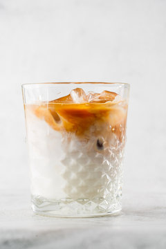 Glass with cold brew coffee and milk isolated on bright marble background. Overhead view, copy space. Advertising for cafe menu. Coffee shop menu. Vertical photo.