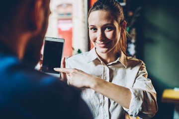 Half length portrait of successful female blogger pointing on mobile application installed on smartphone.Positive young woman recommended website with useful information showing on modern cellular