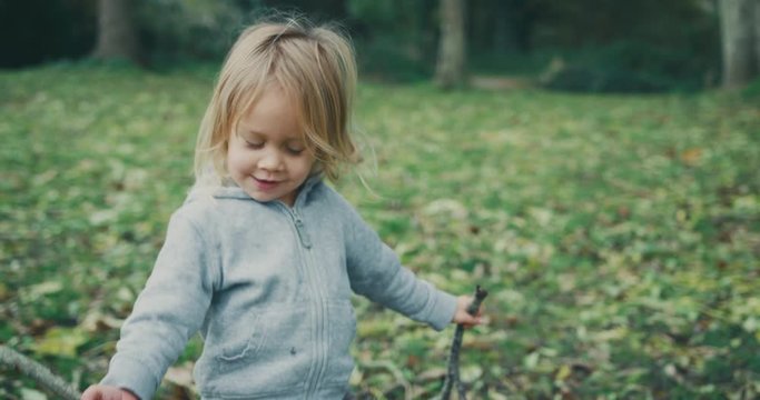 Little toddler standing in the woods with some sticks