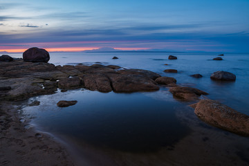 Fototapeta na wymiar Sunset sky over stones and flat rock sinking under Baltic sea. Amazing wilderness of Estonia.